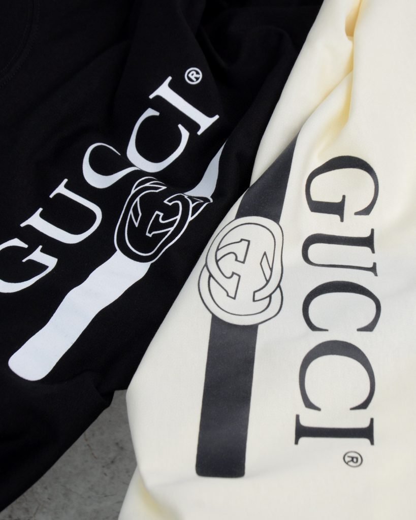 Gucci（グッチ） コピー 芸能人  ベルトロゴダブルgテーププリントラウンドネック半袖Tシャツ